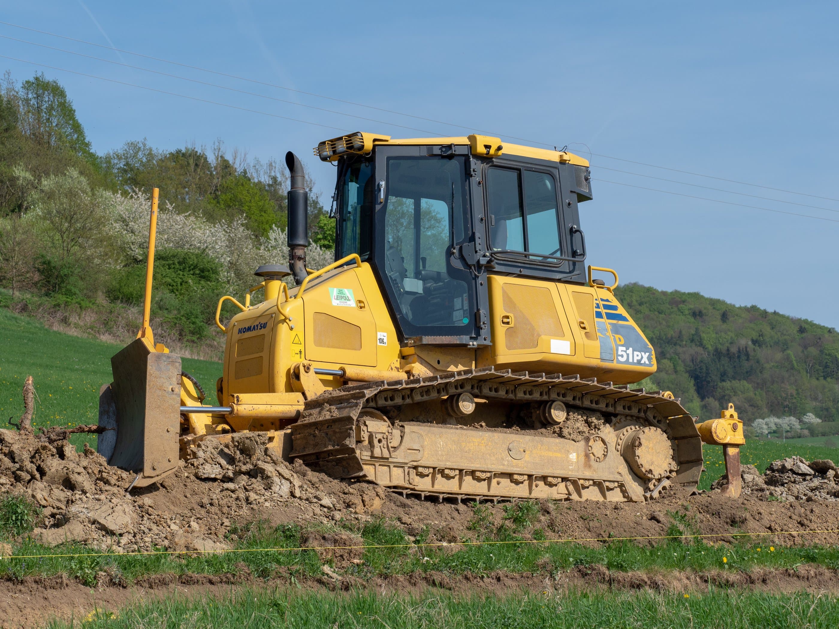 Trator de esteira Komatsu D51PX com lâmina, sobre terra recém-movimentada em área de terraplenagem, com mata ao fundo
